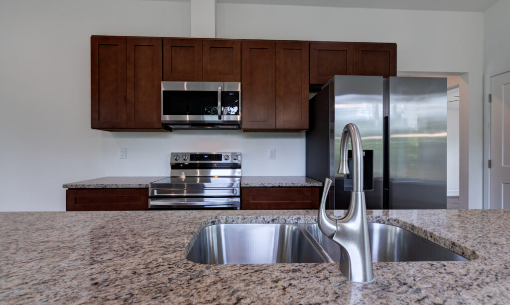 kit home kitchen granite island with kitchen faucet and dark wood cabinets with stainless steel appliances