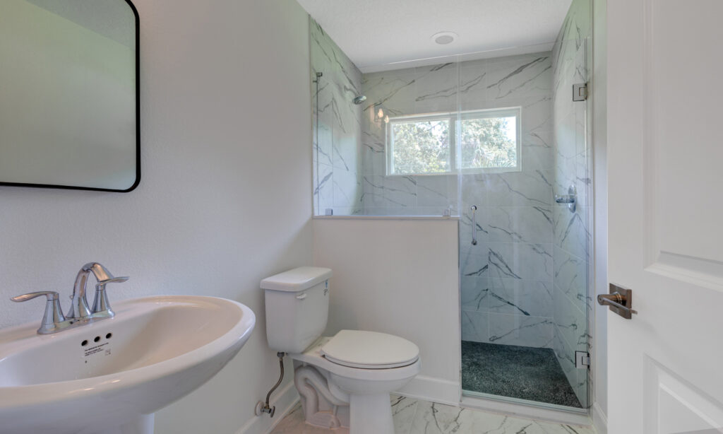 kit home bathroom with glass shower enclosure and white and grey streaked marble walls